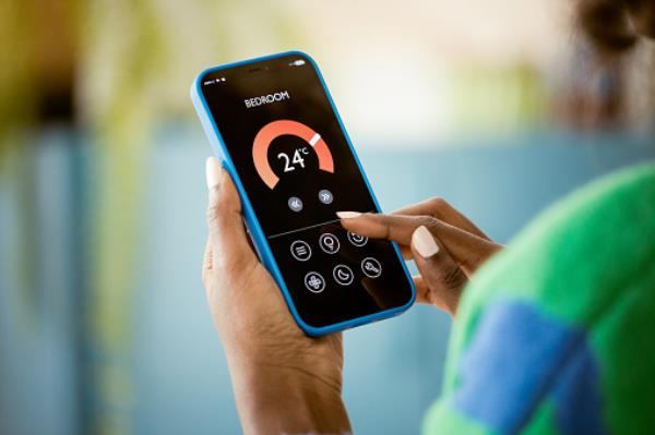 Woman using mobile phone to co<em></em>ntrol termostat at home