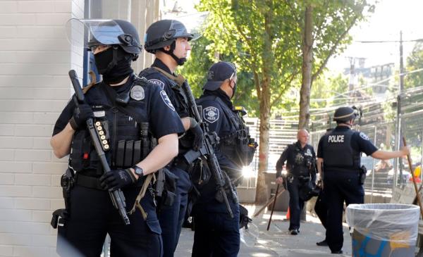Seattle Police officers hold weapons as they stand guard outside the East Precinct Building, Sunday, July 19, 2020 in Seattle. 