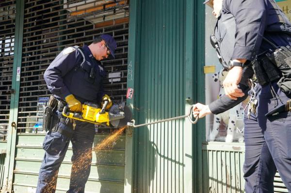 An NYPD officer uses a saw to cut through a padlock at the locked Zaza Waza store on Columbus Ave. in Manhattan on March 14, 2024.