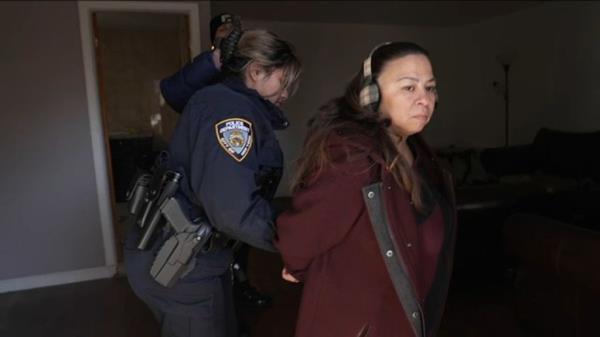A woman accompanied by a police officer entering her disputed property, with signs of surprised recognition on her face