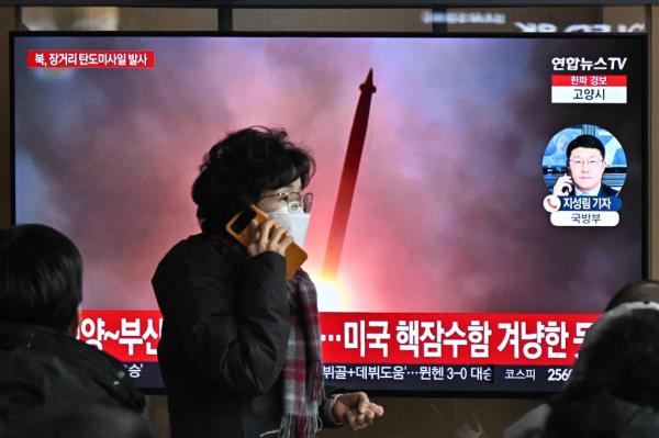 A woman walks past a television screen showing a news broadcast with file footage of a North Korean missile test at a railway station in Seoul on Dec. 18, 2023. 