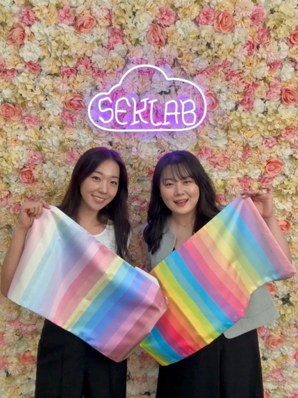 Lily Heo (lefT) and Lizzie Heo hold up color swatches beneath a neon Seklab sign. 