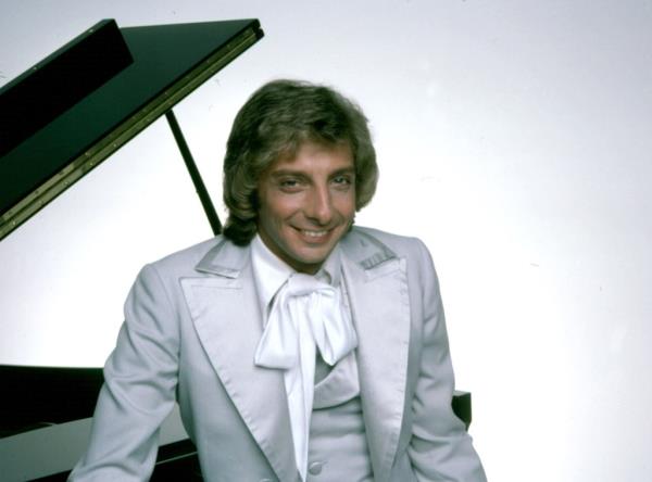 Barry Manilow in white tuxedo in front of grand piano.
