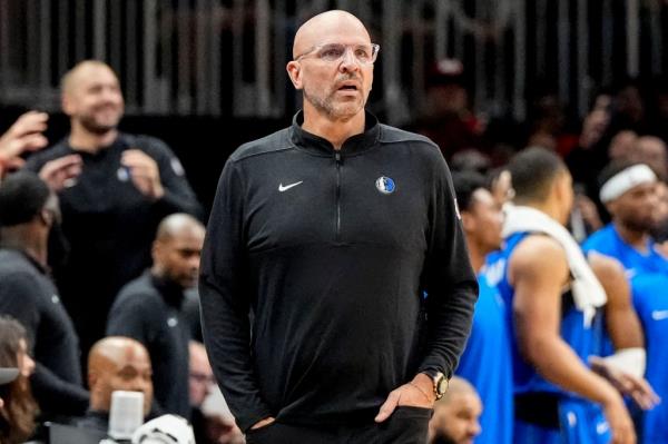 Jason Kidd, head coach of the Dallas Mavericks, watches a basketball game from the sideline, with players visible in the background.