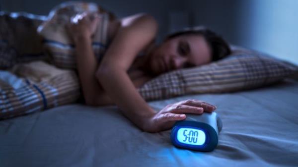 woman hitting alarm clock at 5 a.m. in the dark
