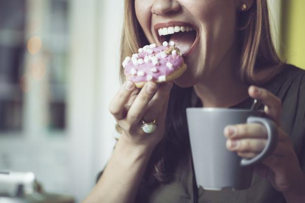 close up of young white woman eating pink frosted do<em></em>nut with her coffee