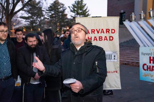 Rabbi Hirschy Zarchi  speaks in front of a menorah and students at Harvard