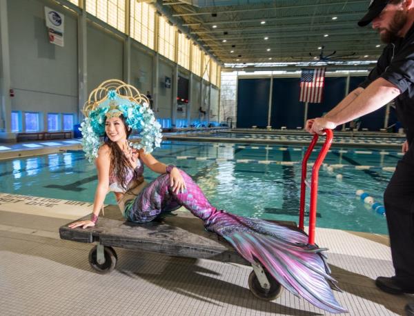 A woman in a mermaid tail by a pool. 