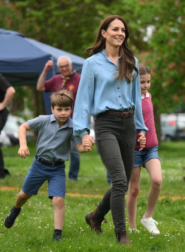 A woman holding the hands of two children in a scout hut while volunteering.