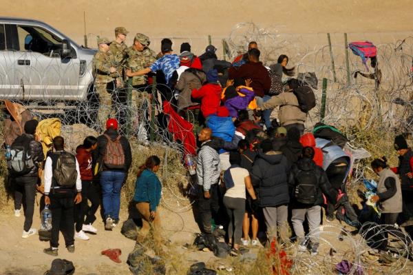 Migrants seeking asylum in the United States try to cross a razor wire fence deployed to inhibit the crossing of migrants into the United States as members of the Texas Natio<em></em>nal Guard stand guard, on the banks of the Rio Bravo River, on the border between the U.S. and Mexico, as seen from Ciudad Juarez, Mexico January 2, 2024.