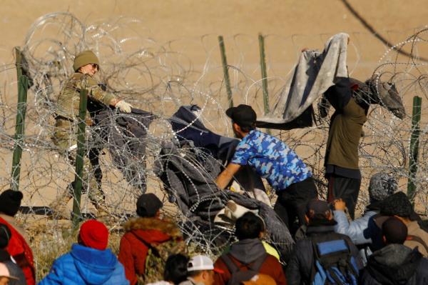 Migrants seeking asylum in the United States try to cross a razor wire fence deployed to inhibit the crossing of migrants into the United States as a member of the Texas Natio<em></em>nal Guard stands guard, on the banks of the Rio Bravo River, on the border between the U.S. and Mexico, as seen from Ciudad Juarez, Mexico January 2, 2024.