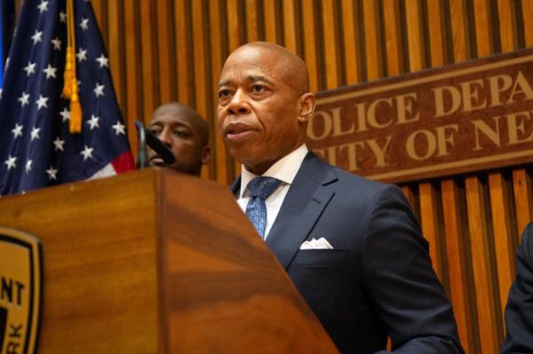 Mayor Eric Adams speaking at a podium at 1 Police Plaza for a press update on the Queens transit stabbings.