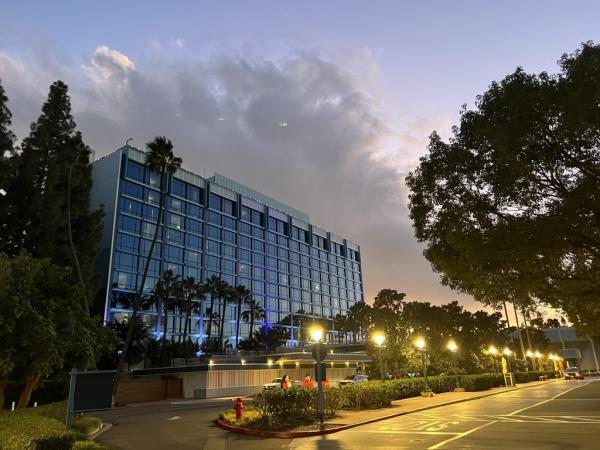 Exterior view of the Disneyland Hotel at twilight with illuminated windows and palm trees.