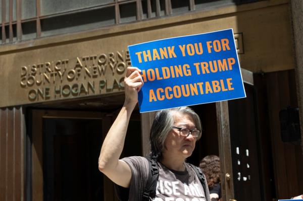 Activist from Rise & Resist group holding a sign thanking Manhattan District Attorney A. Bragg for holding Trump accountable