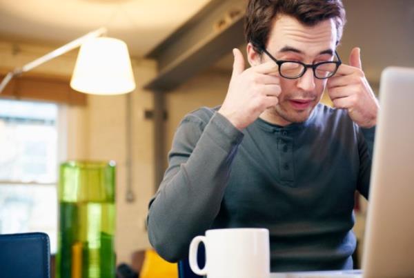 Young man with laptop at home rubbing his eyes