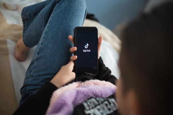 Child lying on the bed at home, holding a phone with TikTok loaded on the screen