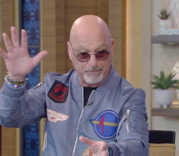 Howie Mandel, wearing sunglasses and a blue jacket with patches, looking distressed