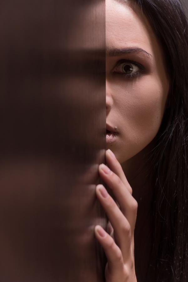 Beautiful young brunette woman looking scared. fear on female face with half face in doorway