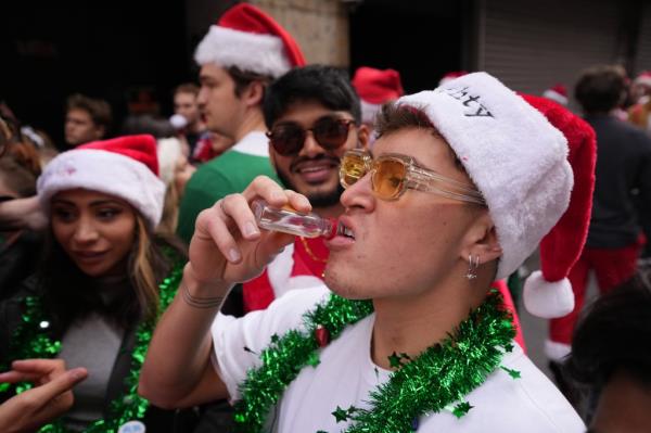 A man drinks a tiny liquor bottle at SantaCon.