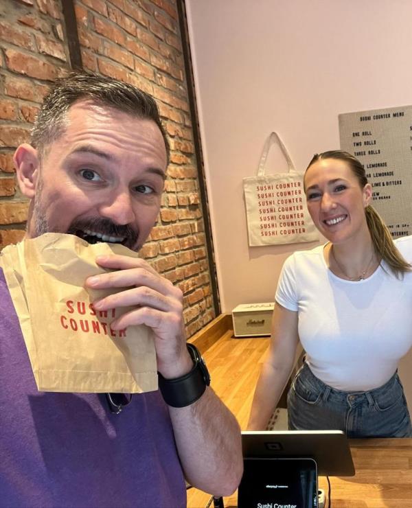 Man biting into sushi roll in Sushi Counter bag while standing next to Alex Marks