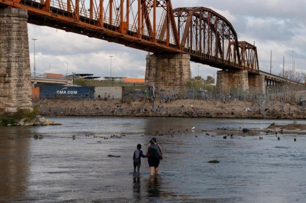 A young Mexican boy holds hands with a Venezuelan migrant as he guides her across the Rio Grande River to the U.S. in Piedras Negras, Mexico.