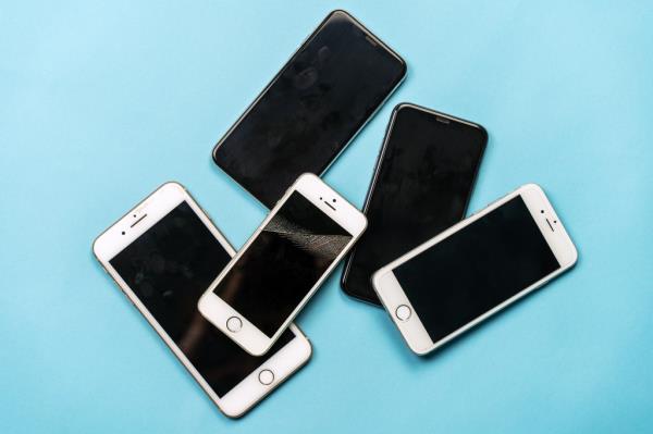 Pile of used, old model black and white mobile pho<em></em>nes with dirty finger spots and broken screens on a blue background