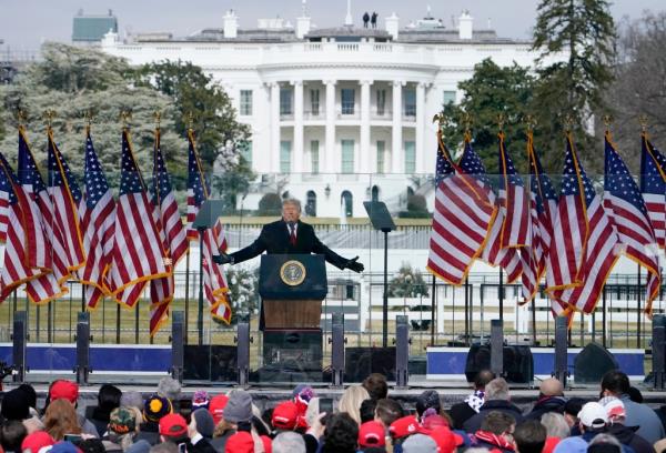 President Do<em></em>nald Trump speaking at a podium with flags, with the White House in the background, during a rally in Washington.