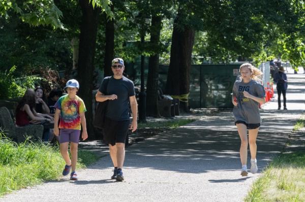 A woman jobs through Prospect Park, passed a father and son walking.