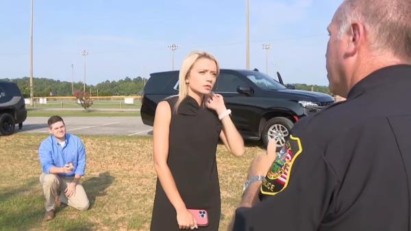 Valerie Bell interviewing a cop as her boyfriend Blake Bjornson waits to propose to her in the background