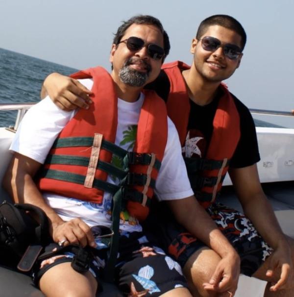 Vidhu's husband, Som, with Rudy when Rudy was an adult. They're on a boat, out at sea, both wearing life jackets and smiling at the camera. Rudy's arm is across Som's shoulders.