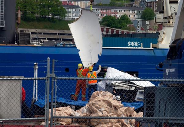 Workers lifting large section of the sub off recovery boat.