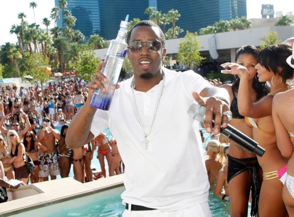 Diddy at a pool party surrounded by bikini clad women next to a pool. 
