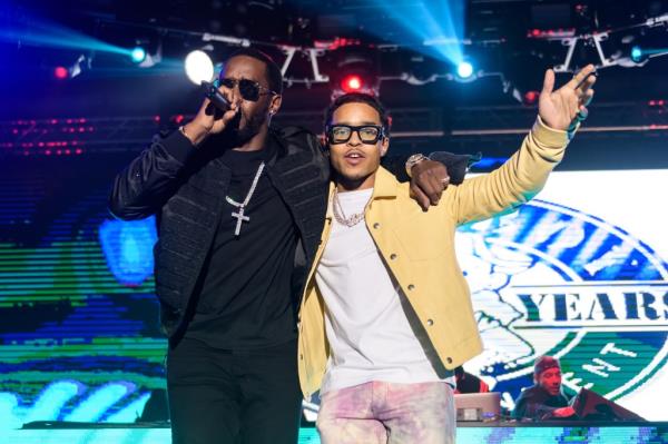Justin on stage with Diddy. Diddy is wearing all blakc, Justin has a yellow jacket and bright pants. 