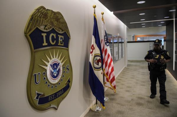 Law enforcement officer walking past ICE logo in a hallway decorated with flags at U.S. Immigration and Customs Enforcement headquarters in Washington, DC