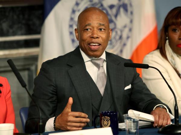 New York City Mayor Eric Adams sitting down at a microphone during a press conference.