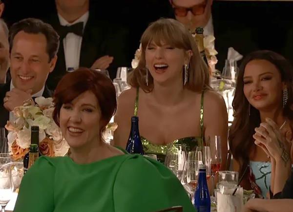 Taylor Swift laughing, sitting at a Golden Globes table. 