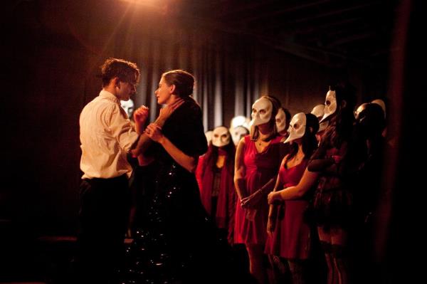 Two performers dance as masked audience members look on at 