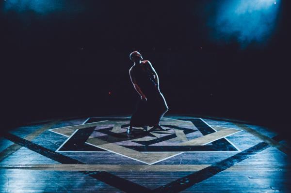 A bald performer poses dramatically in the middle of a stage at 