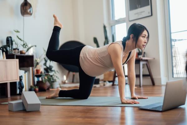 Pregnant woman joining o<em></em>nline fitness class and doing exercise at home