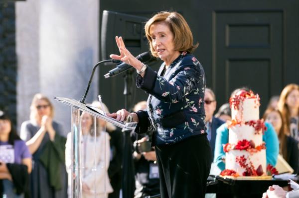 Nancy Pelosi speaking at a microphone before a crow