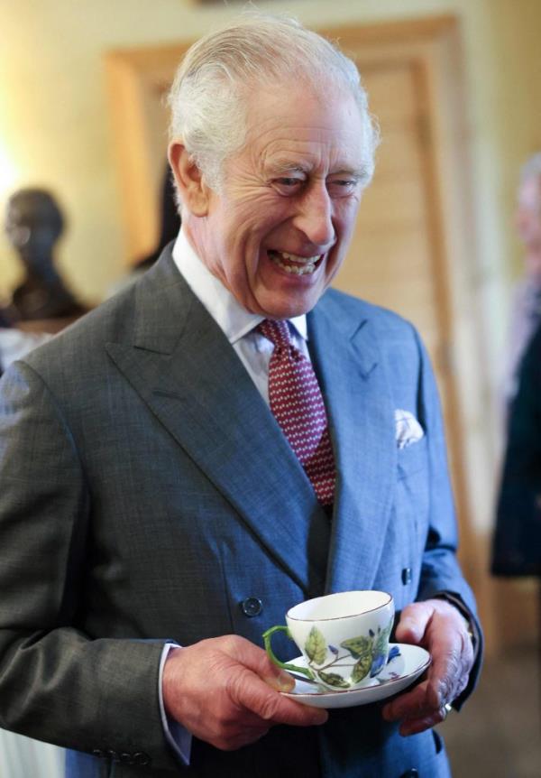 Britain's King Charles III reacts whilst holding a cup and saucer.
