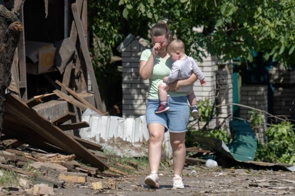 A woman cries as she carries her child, leaving the scene of a Russian rocket attack that ruined her house in Stari Petrivtsi close to Kyiv, Ukraine, Friday, June 16, 2023. 