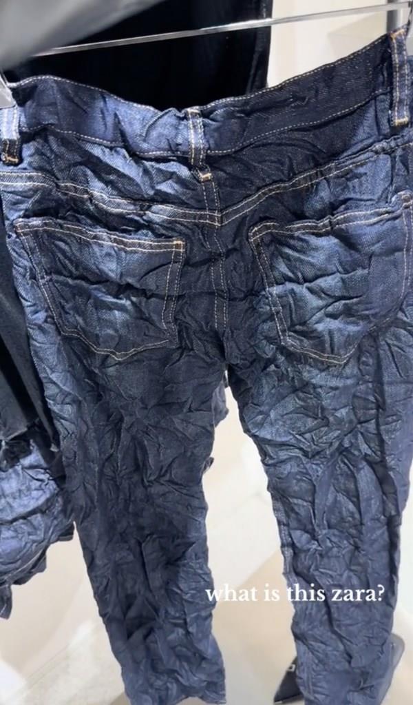 TRF Creased-effect Mid-rise Jeans, dark-wash with creased design & me<em></em>tal button fastening, hanging in a store.
