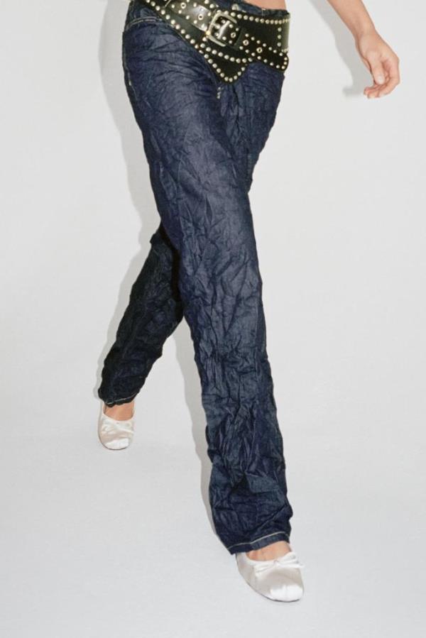 A pair of TRF Creased-effect Mid-rise Jeans by Zara on a person's legs. The pants have a wet creased design with five pockets and a button fastening.