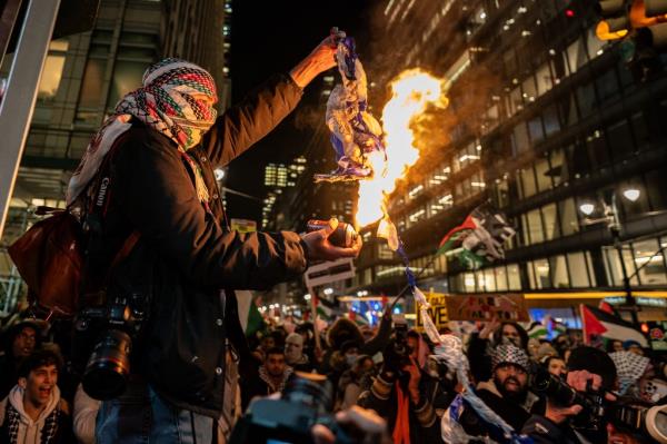 A Pro-Palestine supporter burns an Israeli flag during a rally near the Rockefeller tree lighting on November 29, 2023 in New York City.