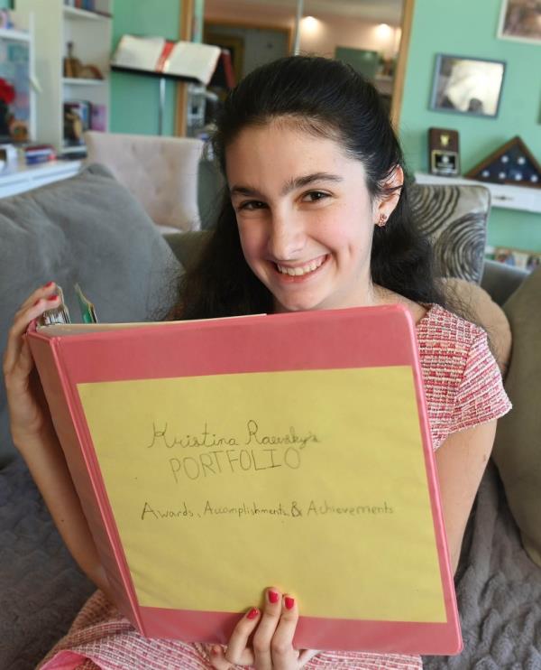 Kristina Raevsky, a 14-year-old girl with a 100 GPA, in her Forest Hills apartment, holding a binder filled with her awards, accomplishments and achievements.