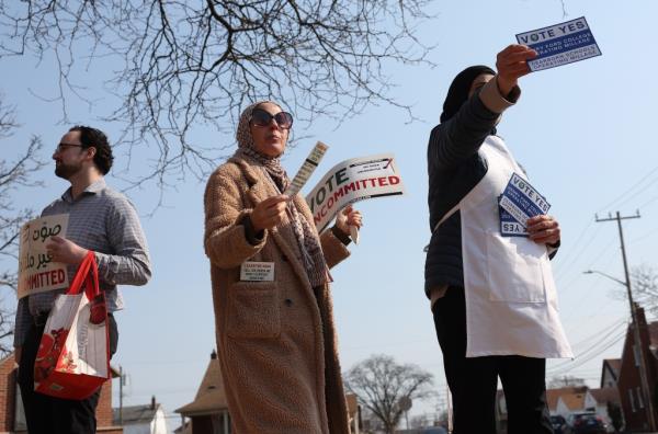 A group of people holding signs outside a polling location for the Michigan primary election in Dearborn, Michigan.