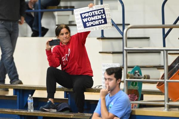 A spectator holds up a Protect Women's Sports sign during the third set of an NCAA college volleyball match between the San Jose State Spartans and the Air Force Falcons