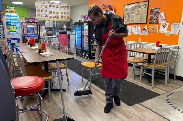 Arriana Dixon, a Kamala Harris supporter, in a red apron sweeping the floor in Johnstown