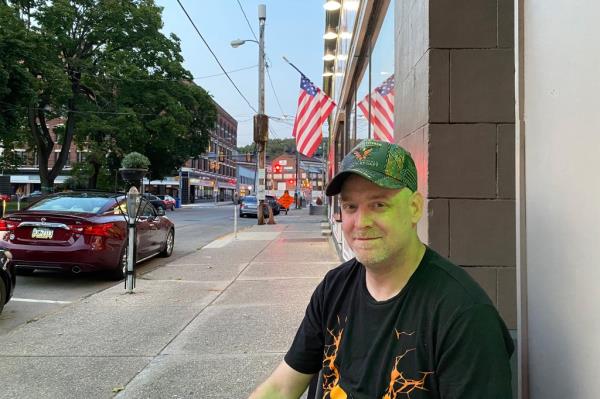 AJ Hasley, a first-time Trump voter, sitting on a sidewalk co<em></em>ntemplating political choices.